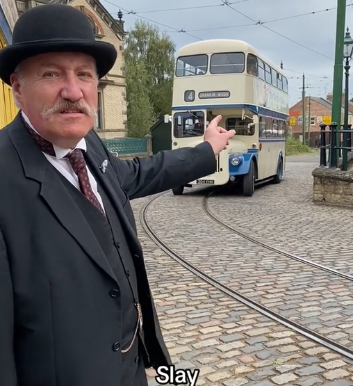 A man in a bowler hat and suit is pointing at an old bus and saying 'Slay', from Beamish Museum's TikTok.